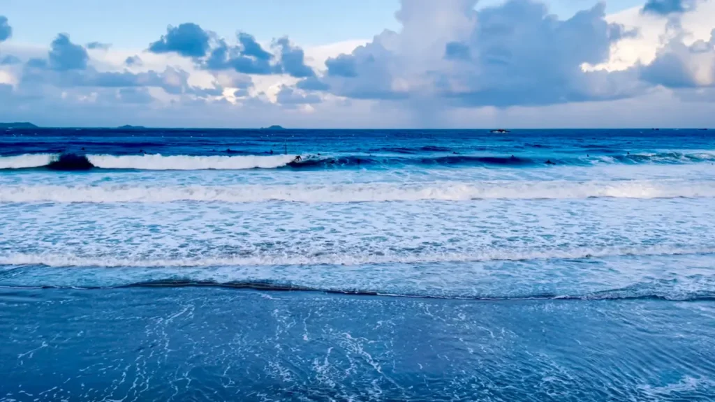 Surfer riding waves at Trestrignel Beach Perros-Guirec with deep blue Atlantic Ocean and dramatic cloudy sky