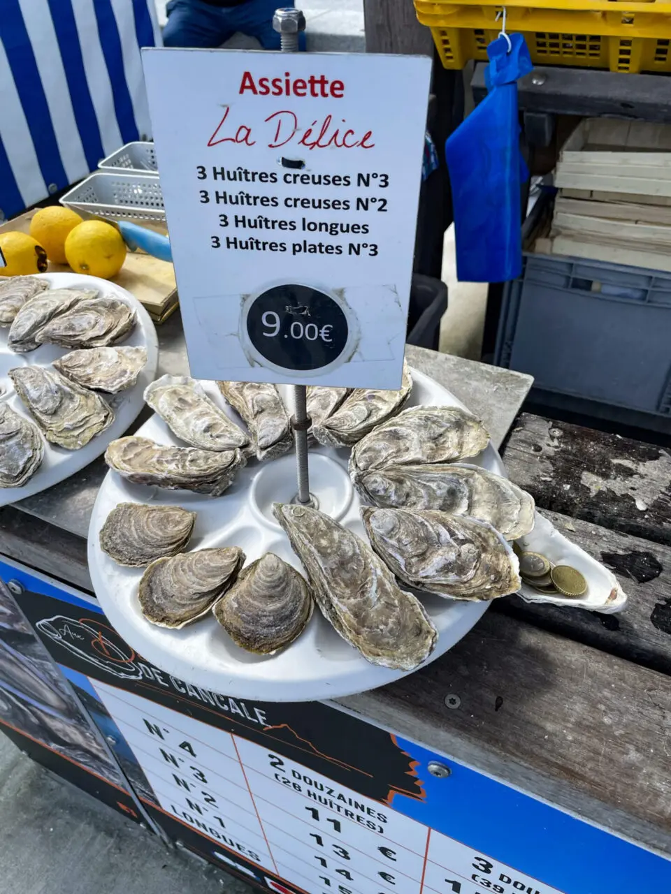 Assiette La Délice oyster tasting plate with 12 fresh Cancale oysters arranged on white plate with lemon and price sign at 9 euros