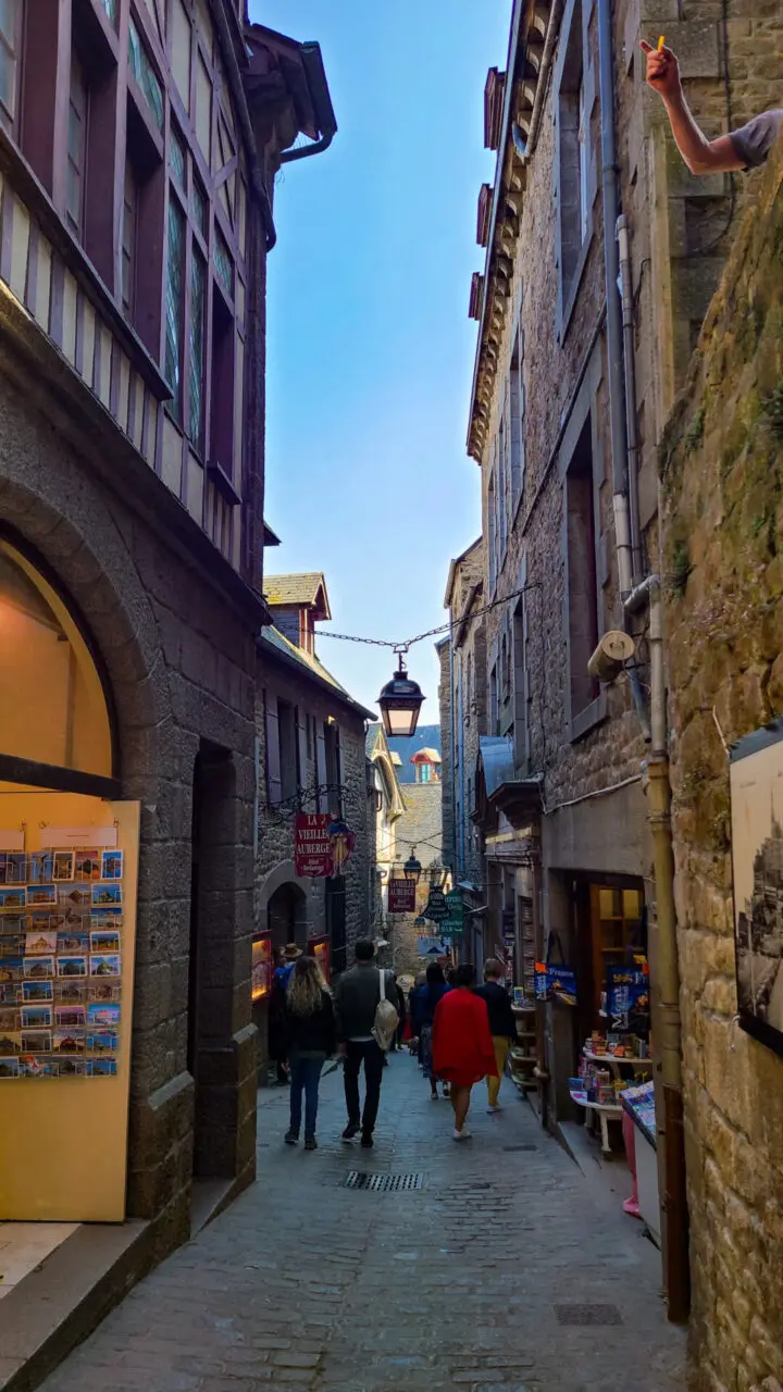 Narrow cobblestone alley inside Mont Saint-Michel with medieval stone buildings and souvenir shops