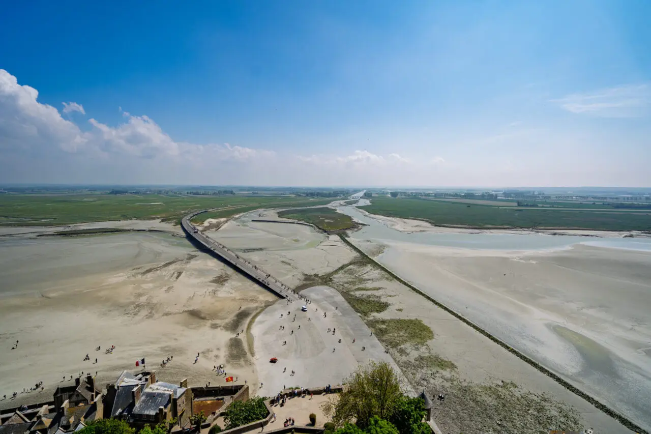 Aerial view from Mont Saint-Michel ramparts showing Passerelle bridge, tidal flats and tiny people below