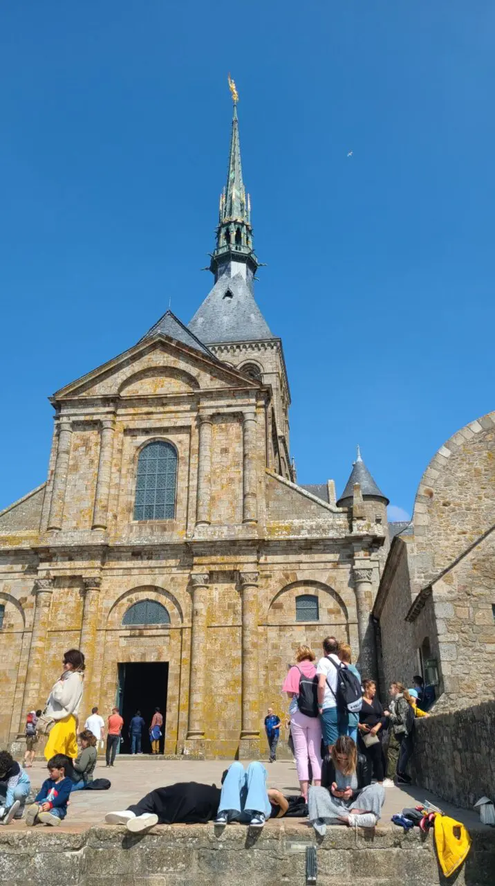 Tourists relaxing and sunbathing on Mont Saint-Michel West Terrace with abbey church in background