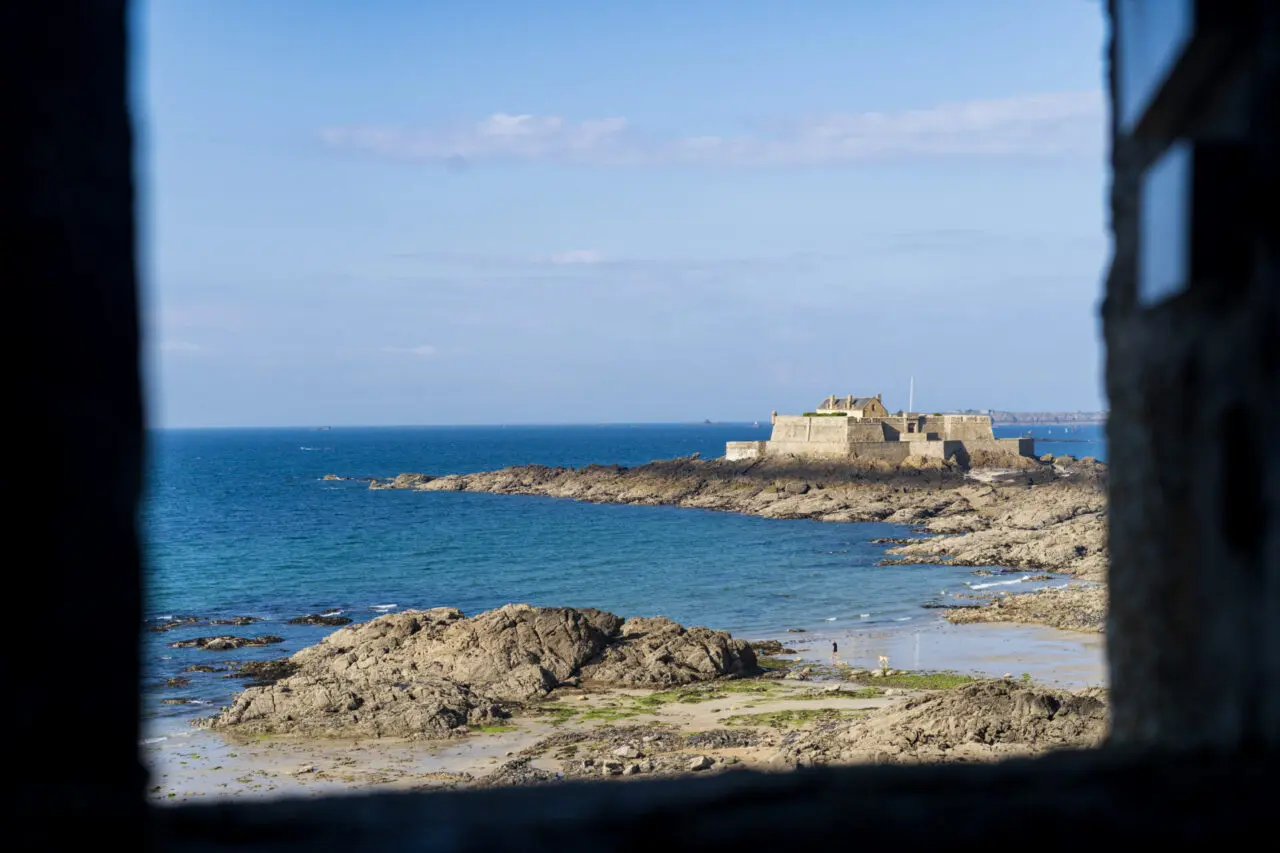Framed view of Petit Bé through hole in Saint-Malo ramparts capturing historic island beyond stone walls